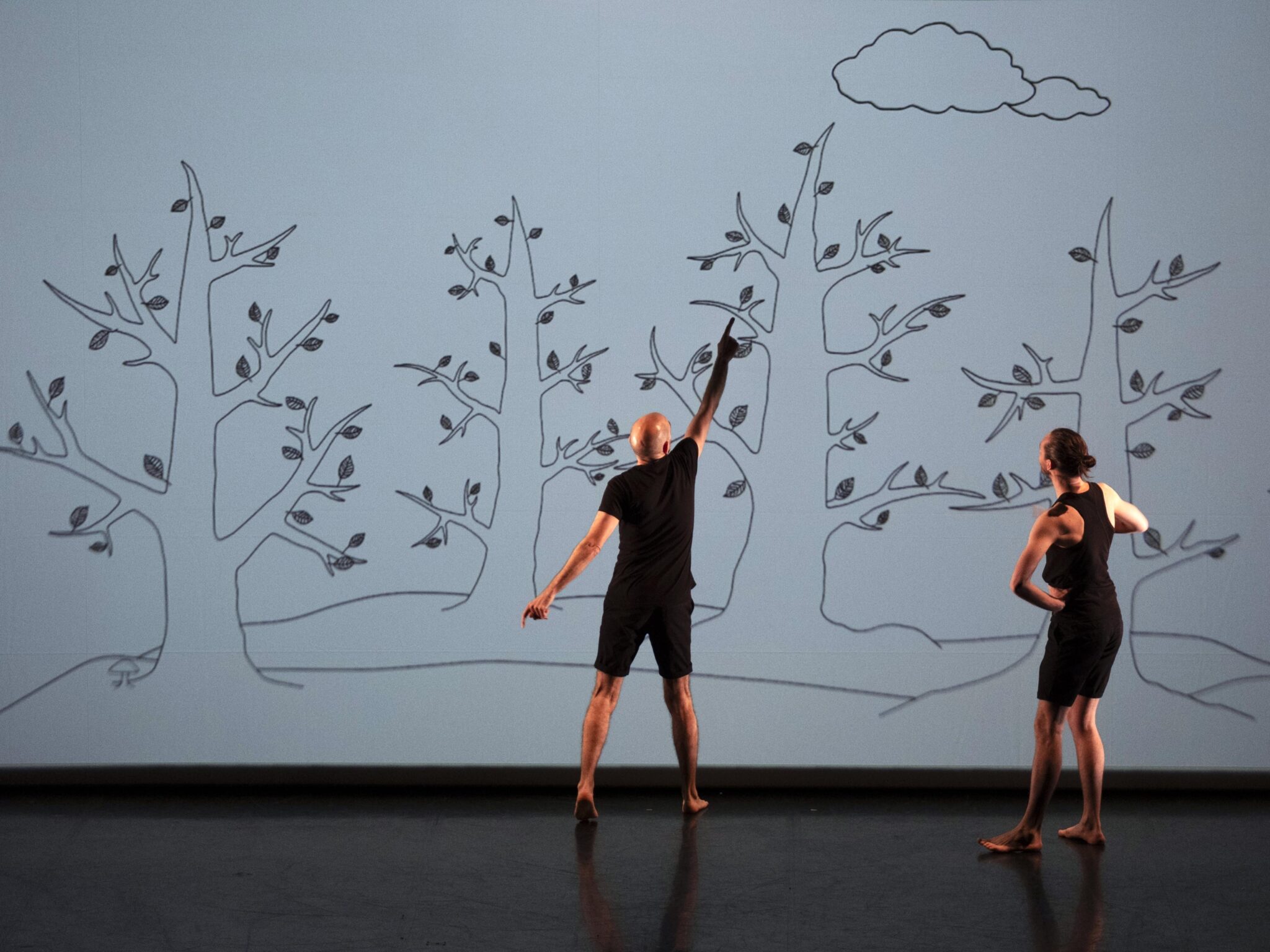 Deux comédiens tournant le dos au public et discutant avec une illustration d'un poisson perché sur un arbre