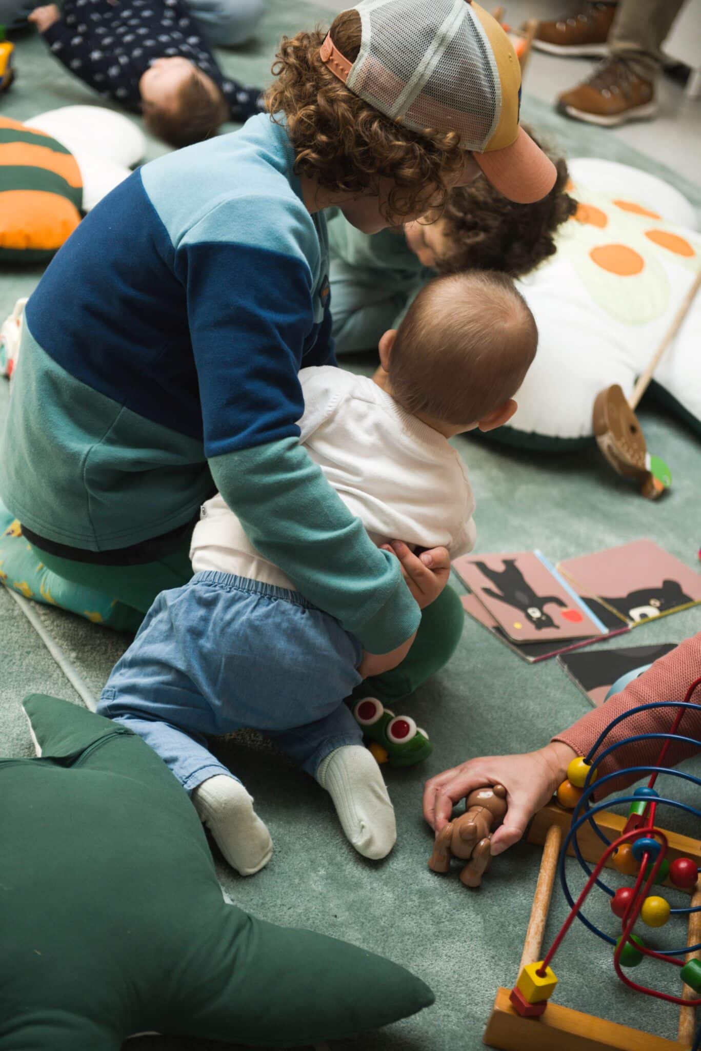 Enfant tenant un autre enfant dans ses bras dans un espace coloré rempli de coussins et d’objets ludiques.