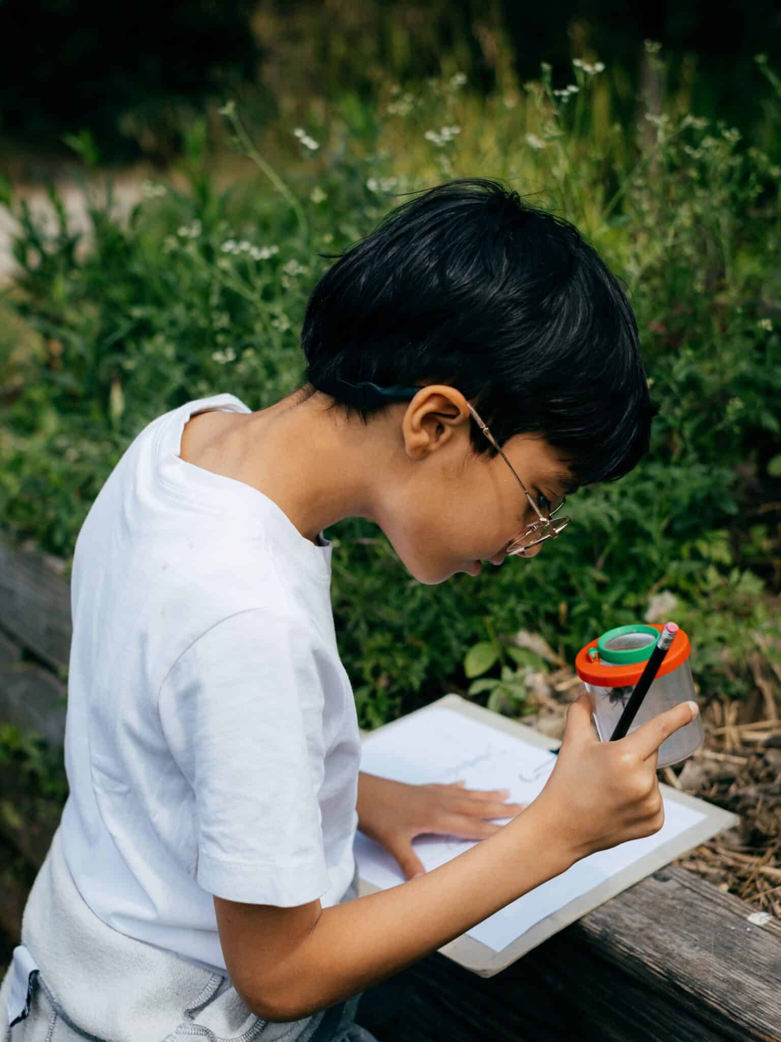 Atelier Les insectes jardiniers dans les jardins passagers de la Villette : un enfant observe un insecte à travers une boite transparente