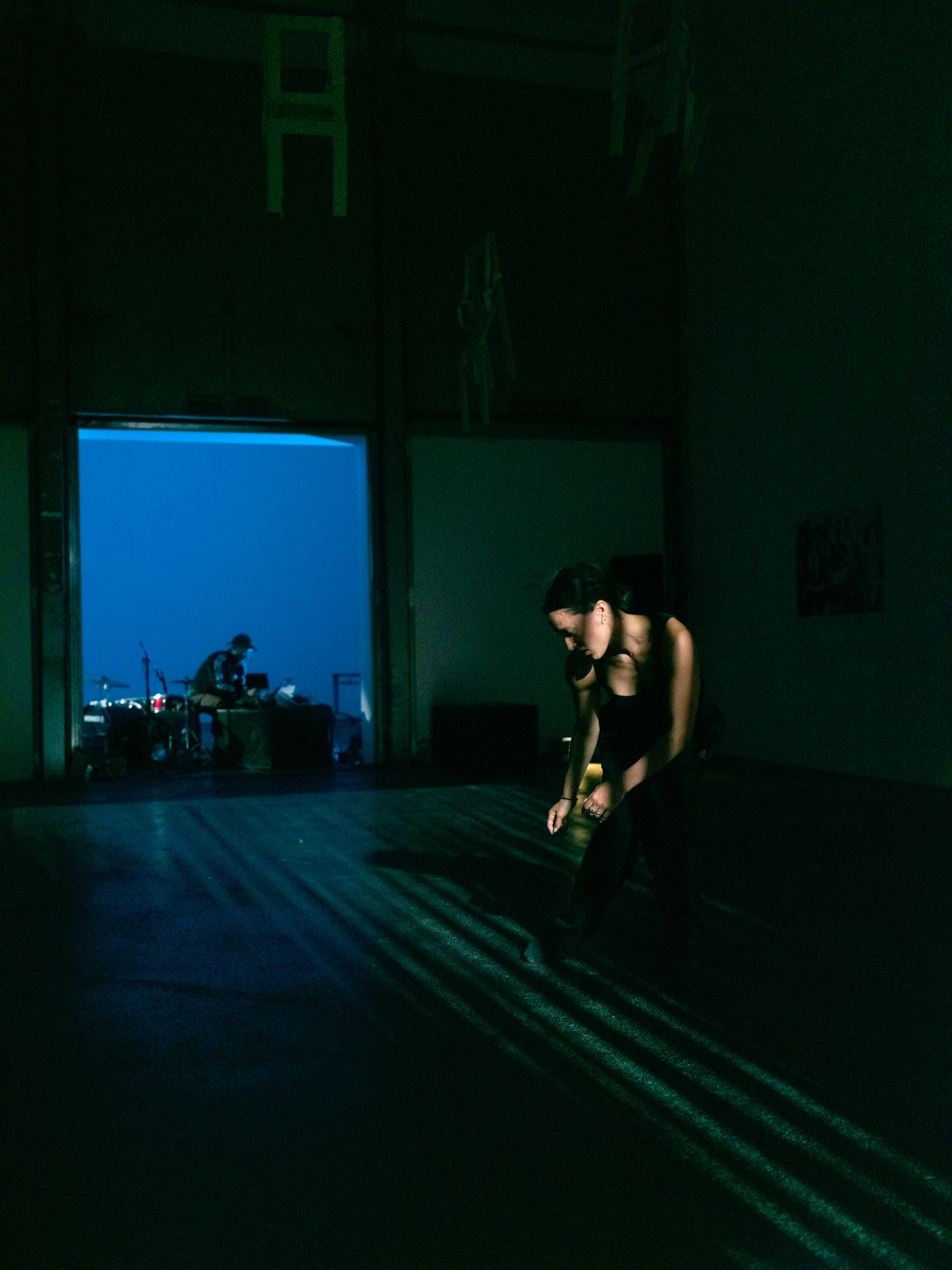 Performance chorégraphique contemporaine à La Villette, une danseuse évolue dans un jeu de lumières, accompagnée par un musicien en arrière-plan.