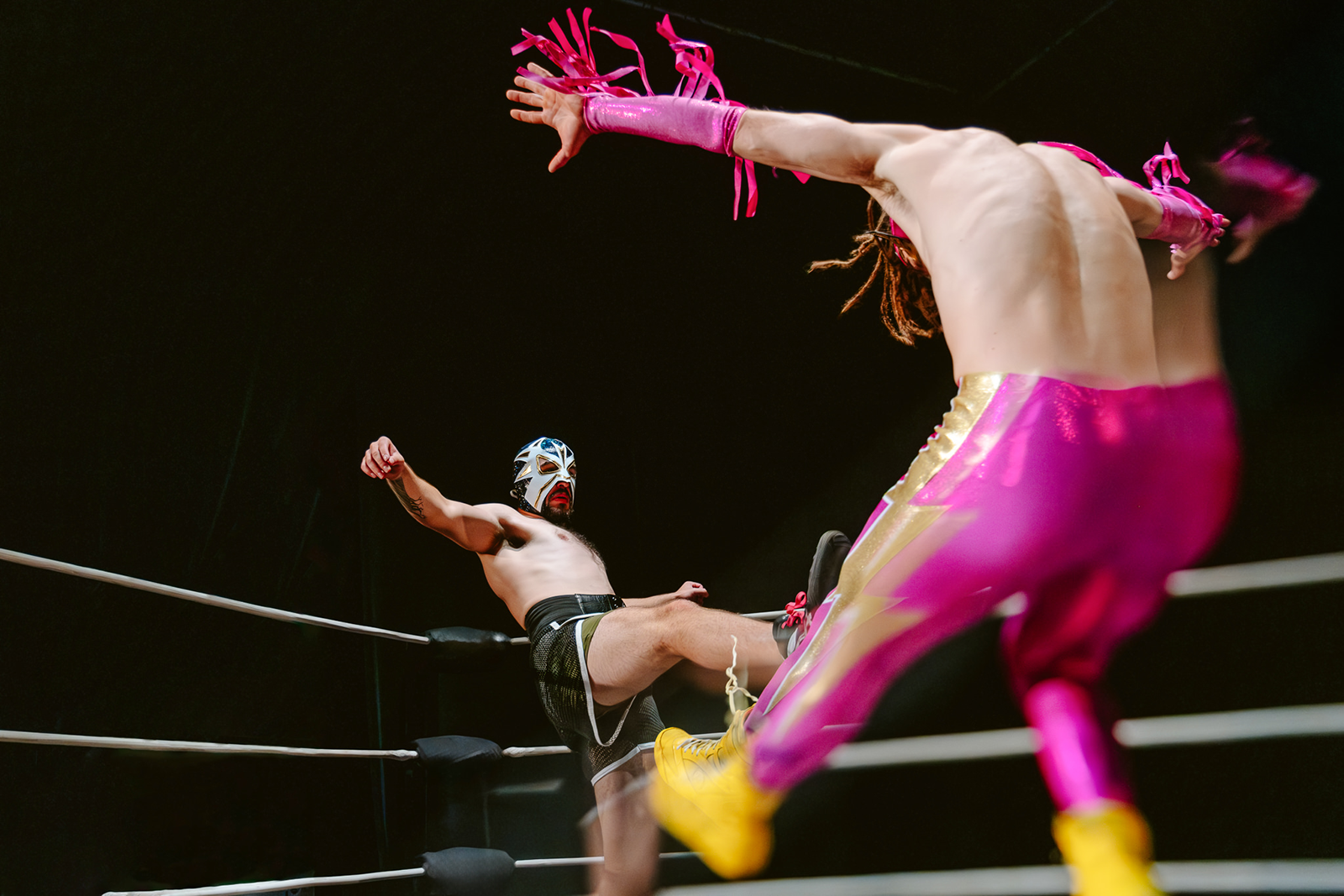 Deux catcheurs en pleine action sur un ring : l’un porte un legging lamé rose, l’autre un masque de Lucha Libre et un short de boxe kaki. Scène tirée du spectacle Slam! de Robert Lepage, FLIP Fabrique et Ex Machina.