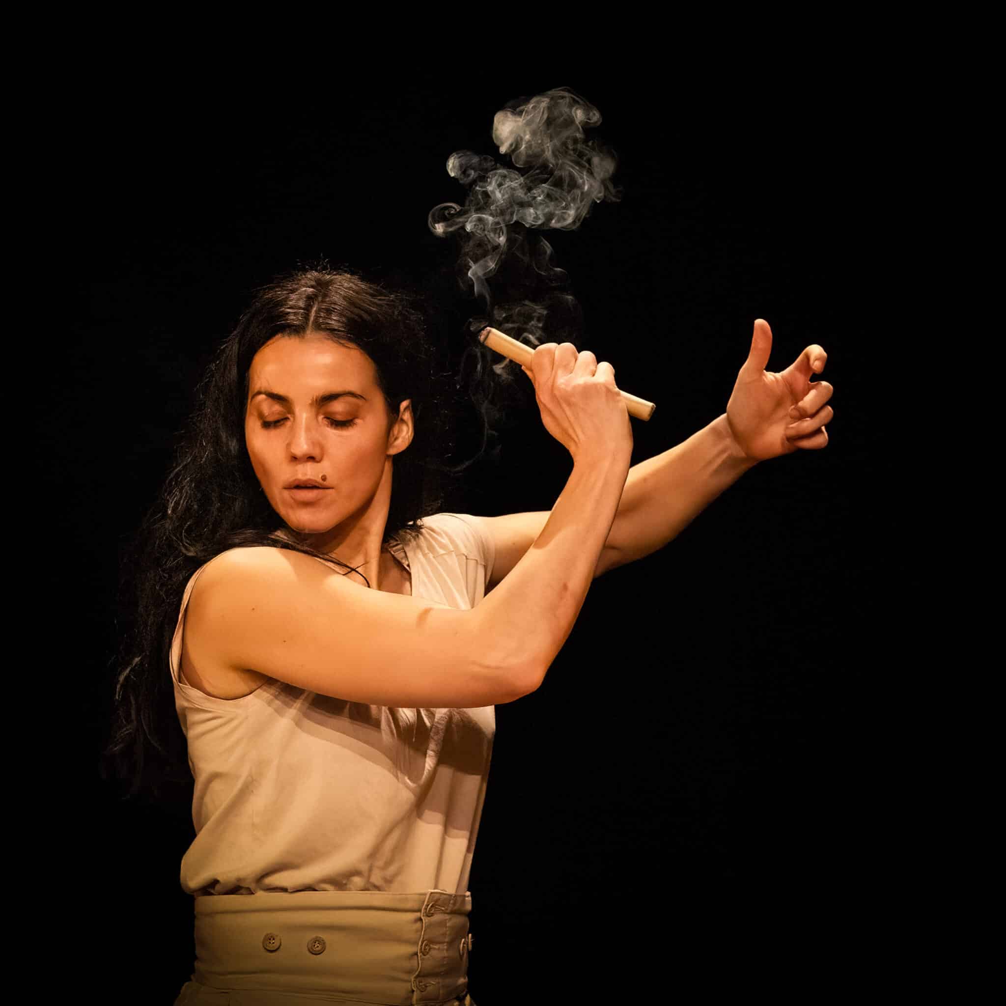Mantra – spectacle de Marlène Gobber : interprète tenant un bâton d’encens d’où s’élève une fumée, en mouvement sur fond noir.