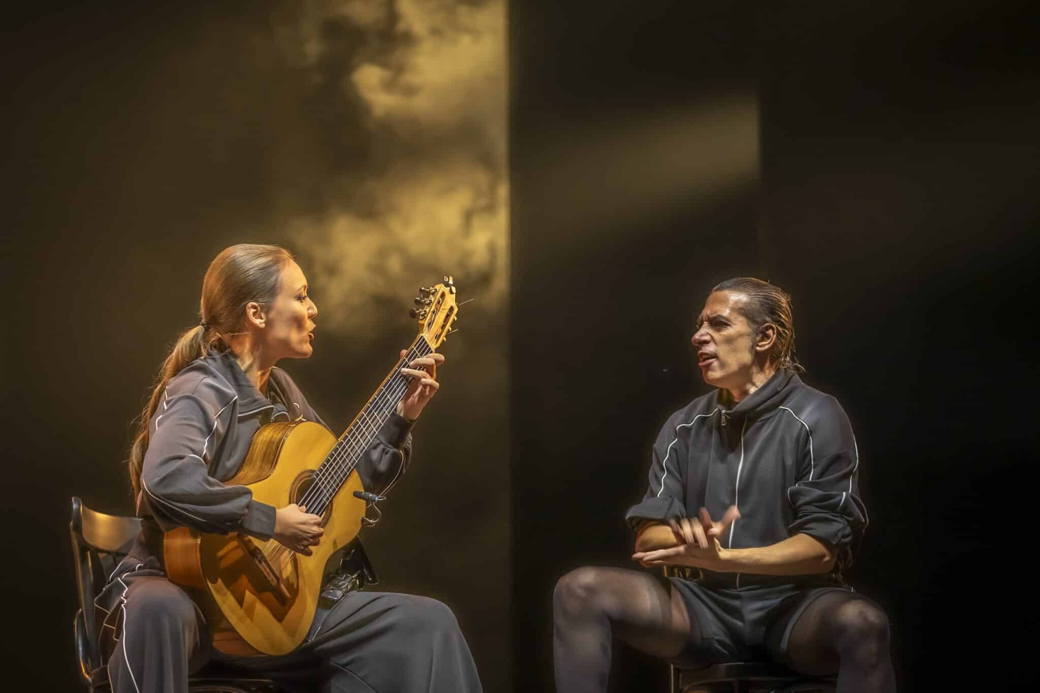 Israel Galván et un guitariste sur scène lors du spectacle Carmen, éclairés par une lumière dorée.