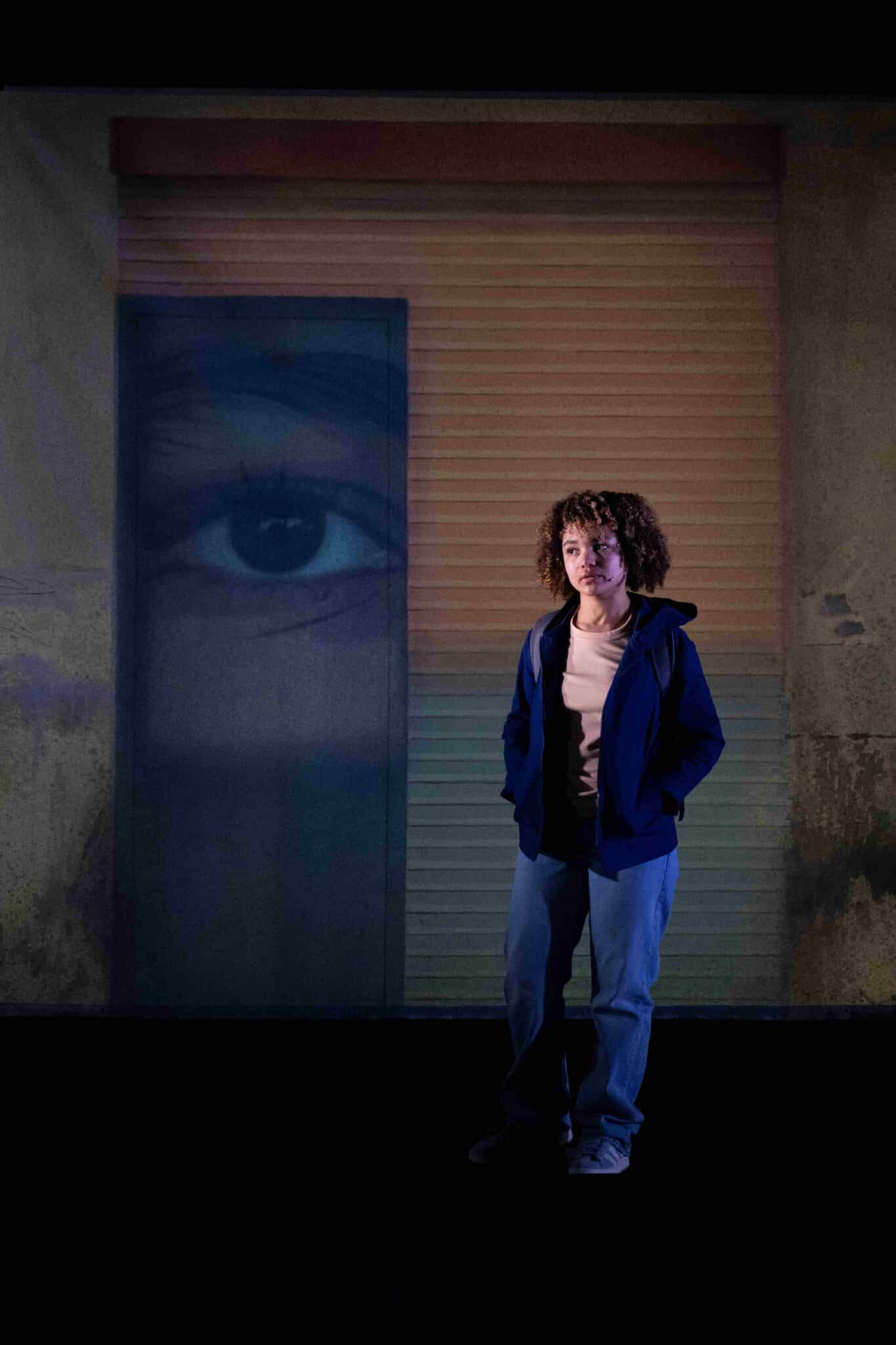 Une interprète sur scène, éclairée en contre-jour, devant une projection d’un œil, dans le spectacle La Petite Tuk de Oh ! Oui Joachim Latarjet et Alexandra Fleischer.