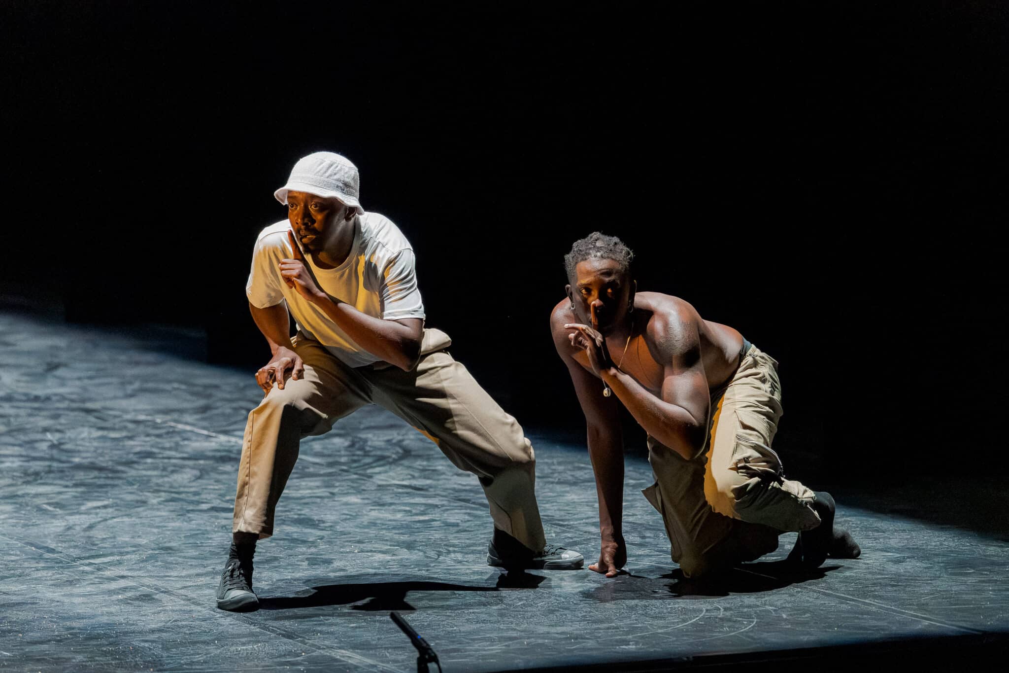 Deux danseurs en posture accroupie sur scène pendant le spectacle Tamujuntu de la compagnie Via Katlehong.