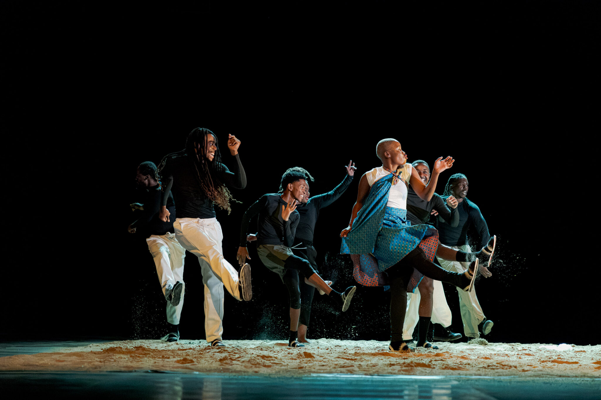 Groupe de danseurs de Tamujuntu interprétant une chorégraphie énergique sur un sol sablé.