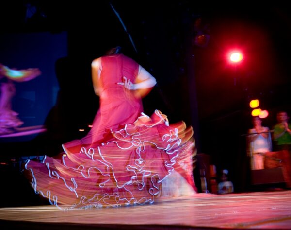 Danseuse de flamenco en robe rouge en mouvement sur une scène éclairée, créant un effet de flou artistique.