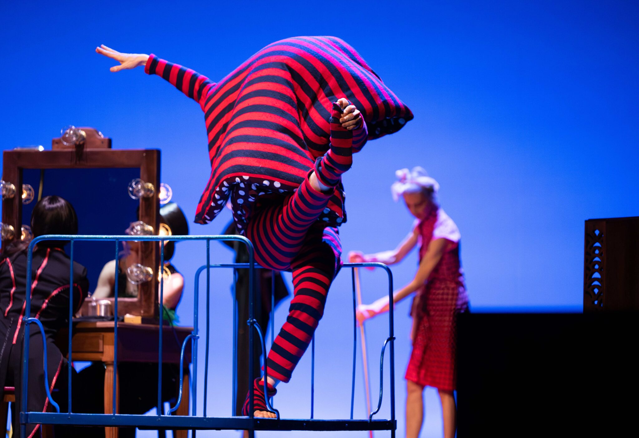 Trois danseurs de la CIE DCA sur scène dans Entre-Temps de Philippe Decouflé, dont l’un porte une tenue rayée rouge et noir.