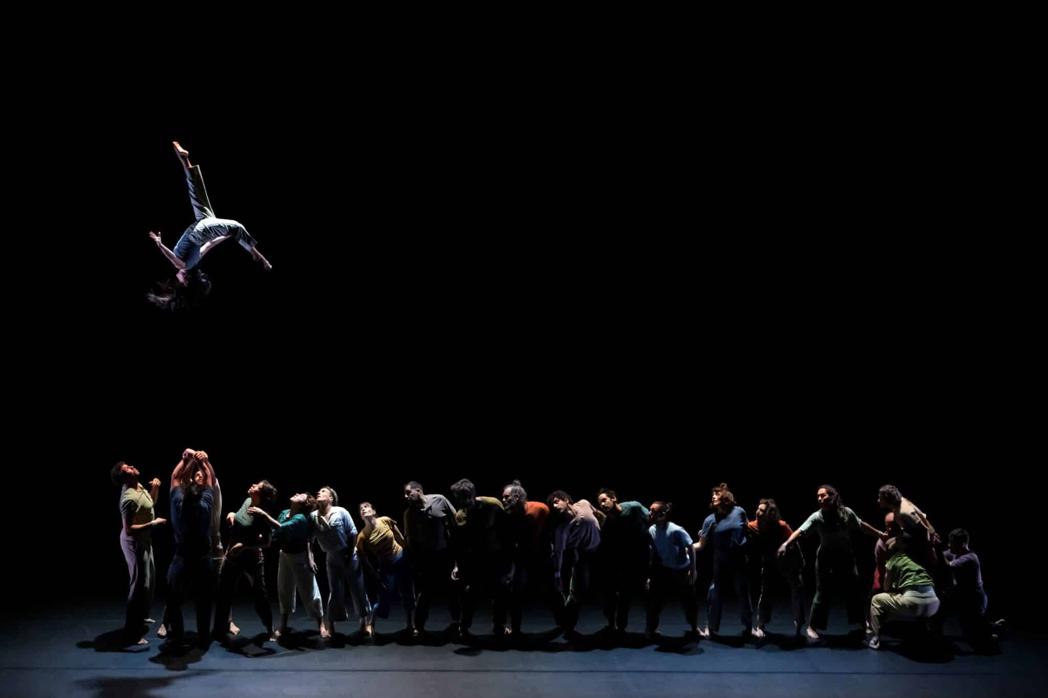Spectacle de cirque à La Villette : un acrobate est projeté dans les airs au-dessus d’un grand groupe d’artistes sur scène.