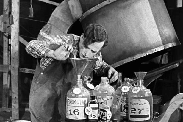 Homme versant un liquide dans un entonnoir, entouré de grandes bouteilles numérotées.