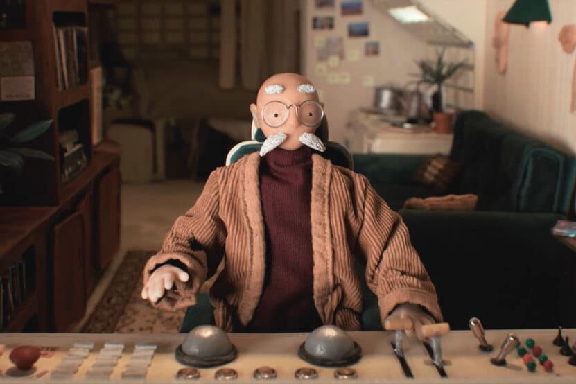 Poupée en stop-motion d’un vieil homme aux commandes d’un tableau de bord dans un salon rétro.