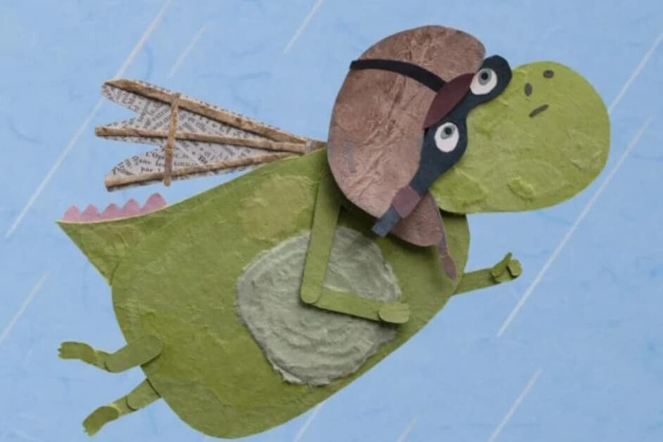 Petit dragon vert en papier volant avec un casque d’aviateur et des ailes en journal.