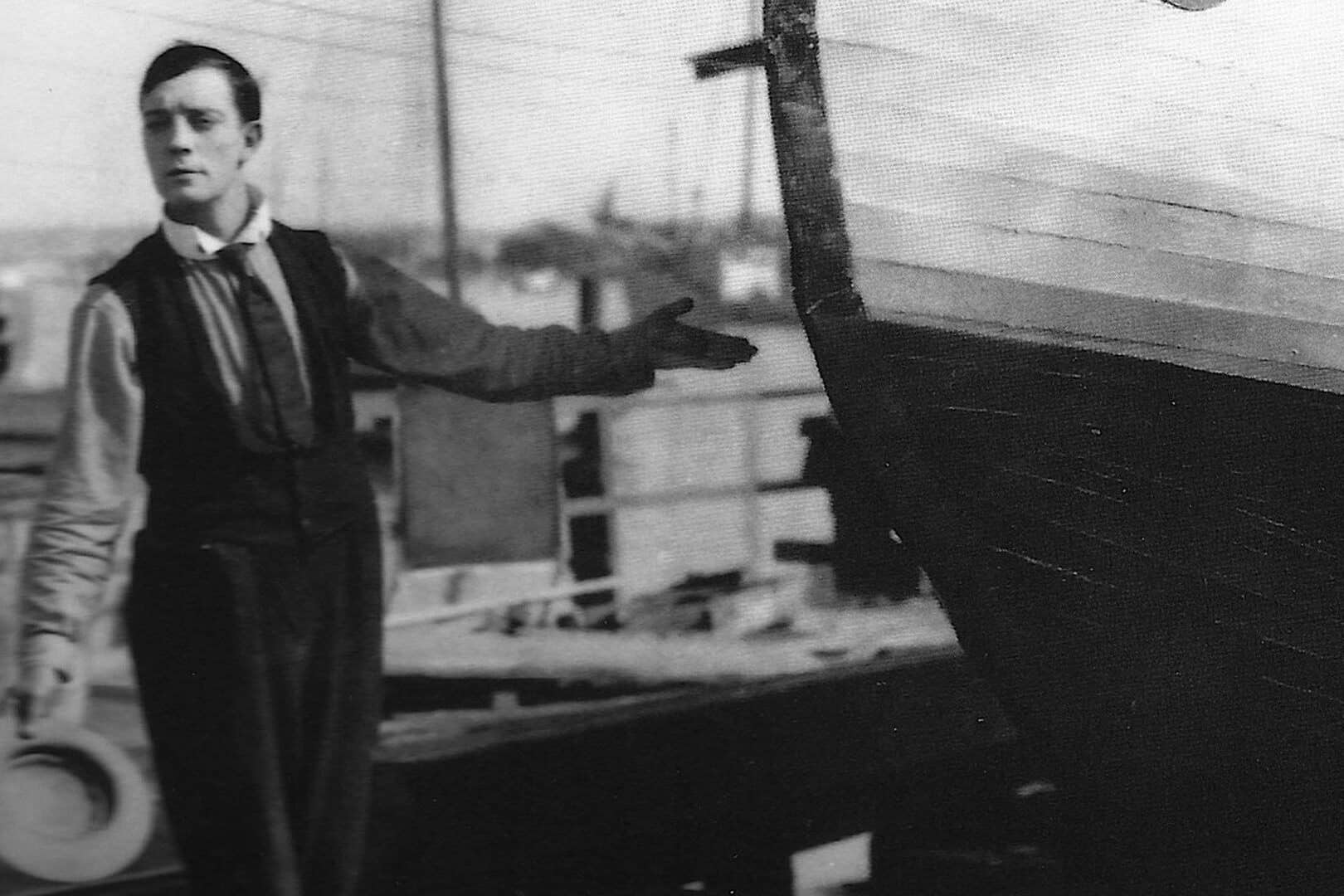 Homme à la barre d’un bateau sous un auvent, en noir et blanc.
