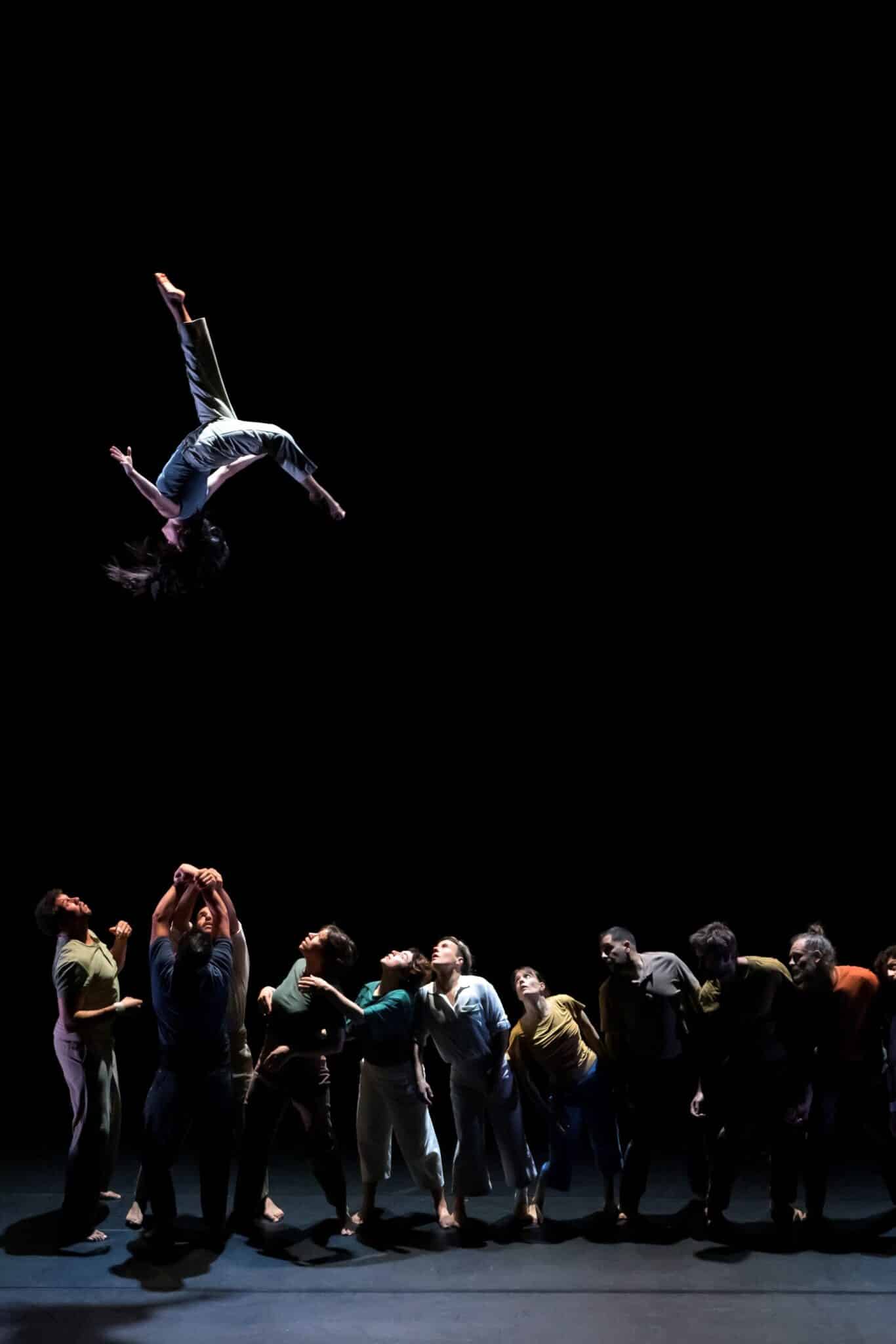 Spectacle de cirque à La Villette : un acrobate est projeté dans les airs au-dessus d’un grand groupe d’artistes sur scène.