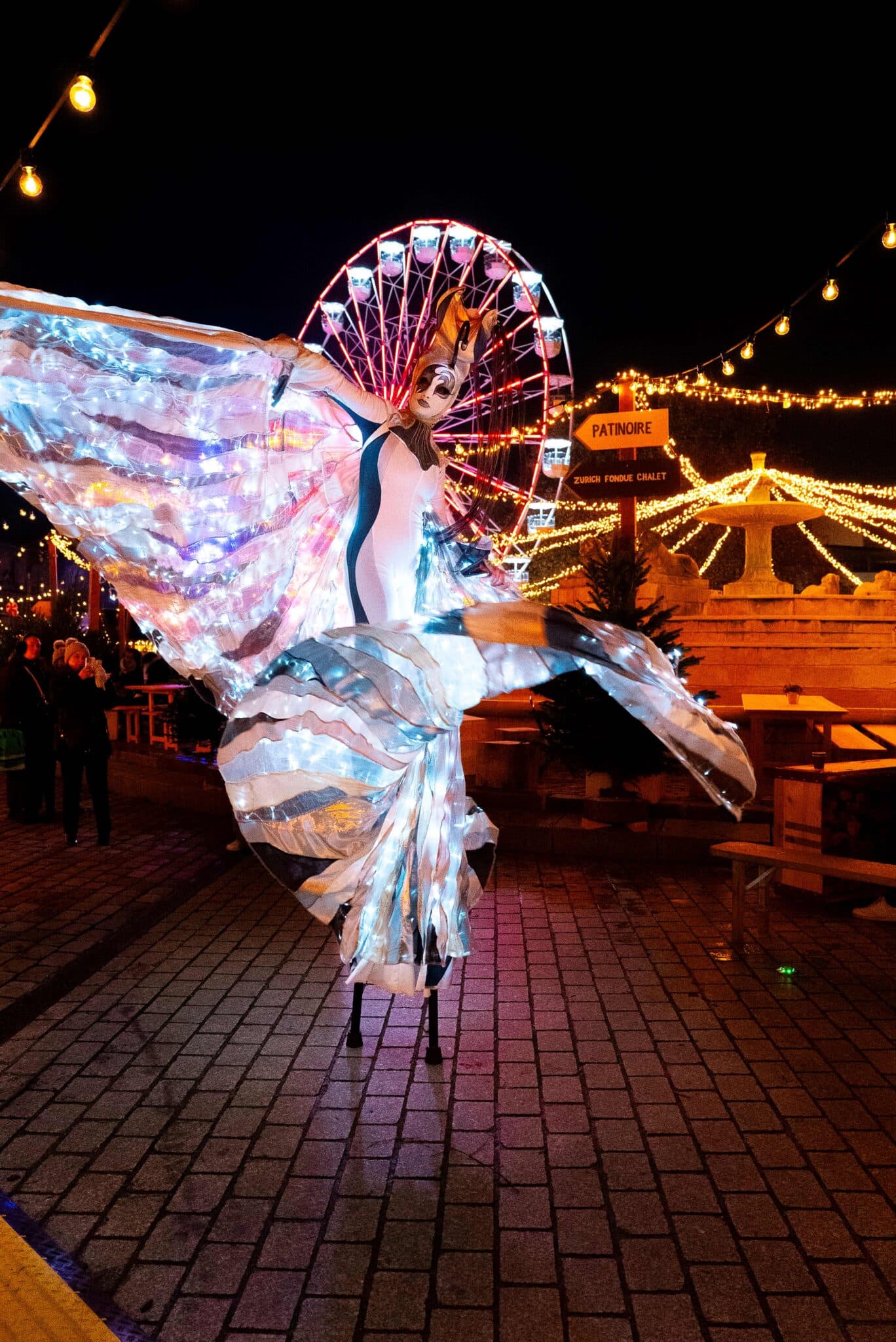 Danseuse en costume lumineux sur des échasses au marché de Noel de La Villette