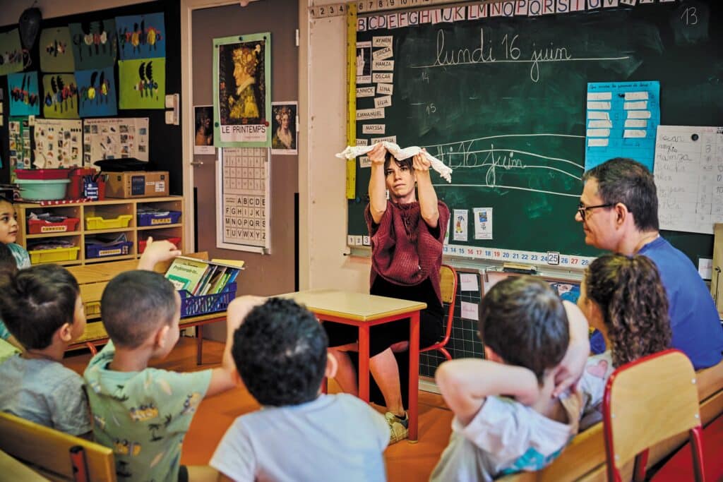 Une intervenante anime un atelier d’éducation artistique et culturelle dans une classe de maternelle, face à un groupe d’enfants attentifs.