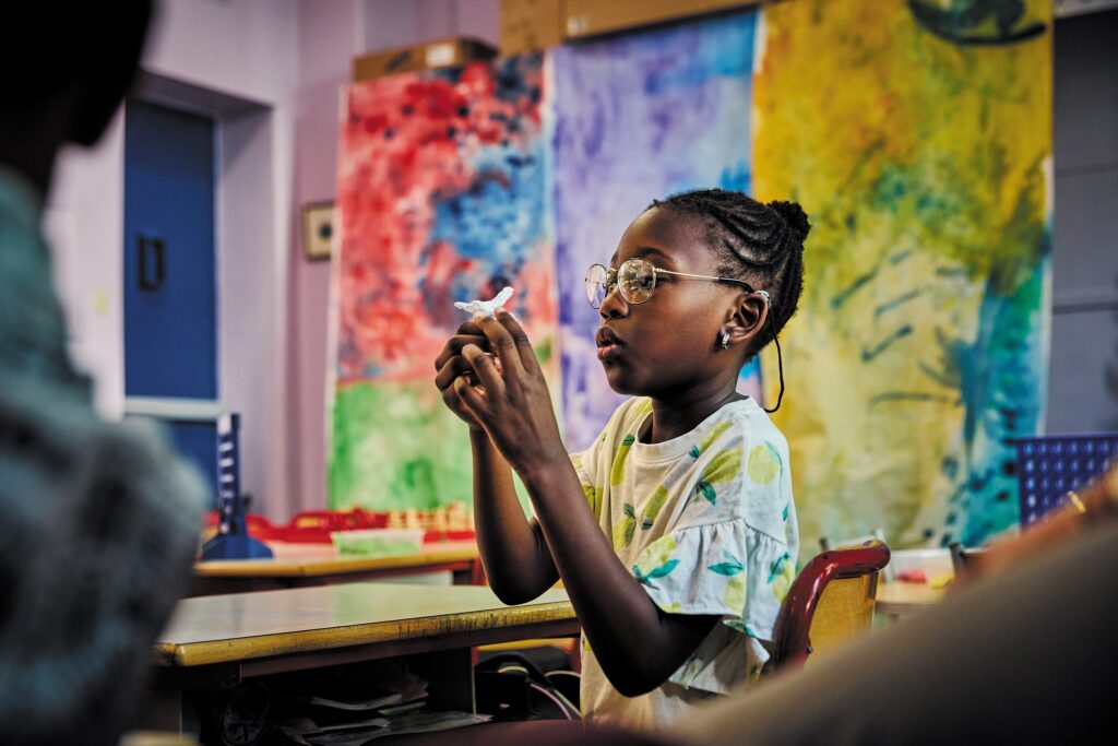 Une élève participe à un atelier d’éducation artistique et culturelle animé par La Villette dans une école, tenant une petite création entre ses mains.